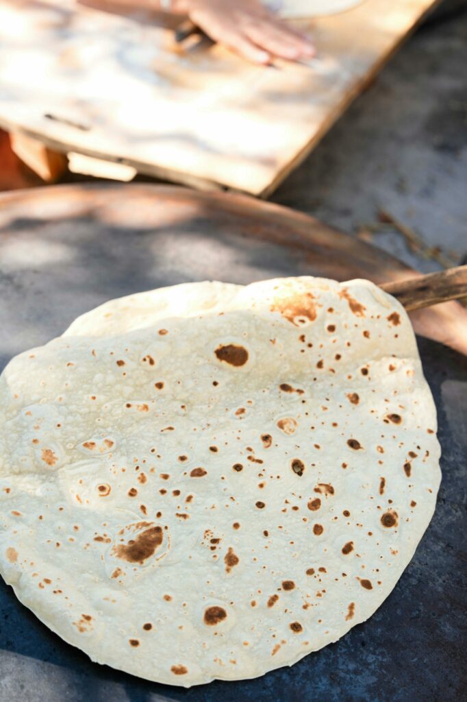 Close-up of flatbread cooking on an outdoor griddle with a baker in the background.